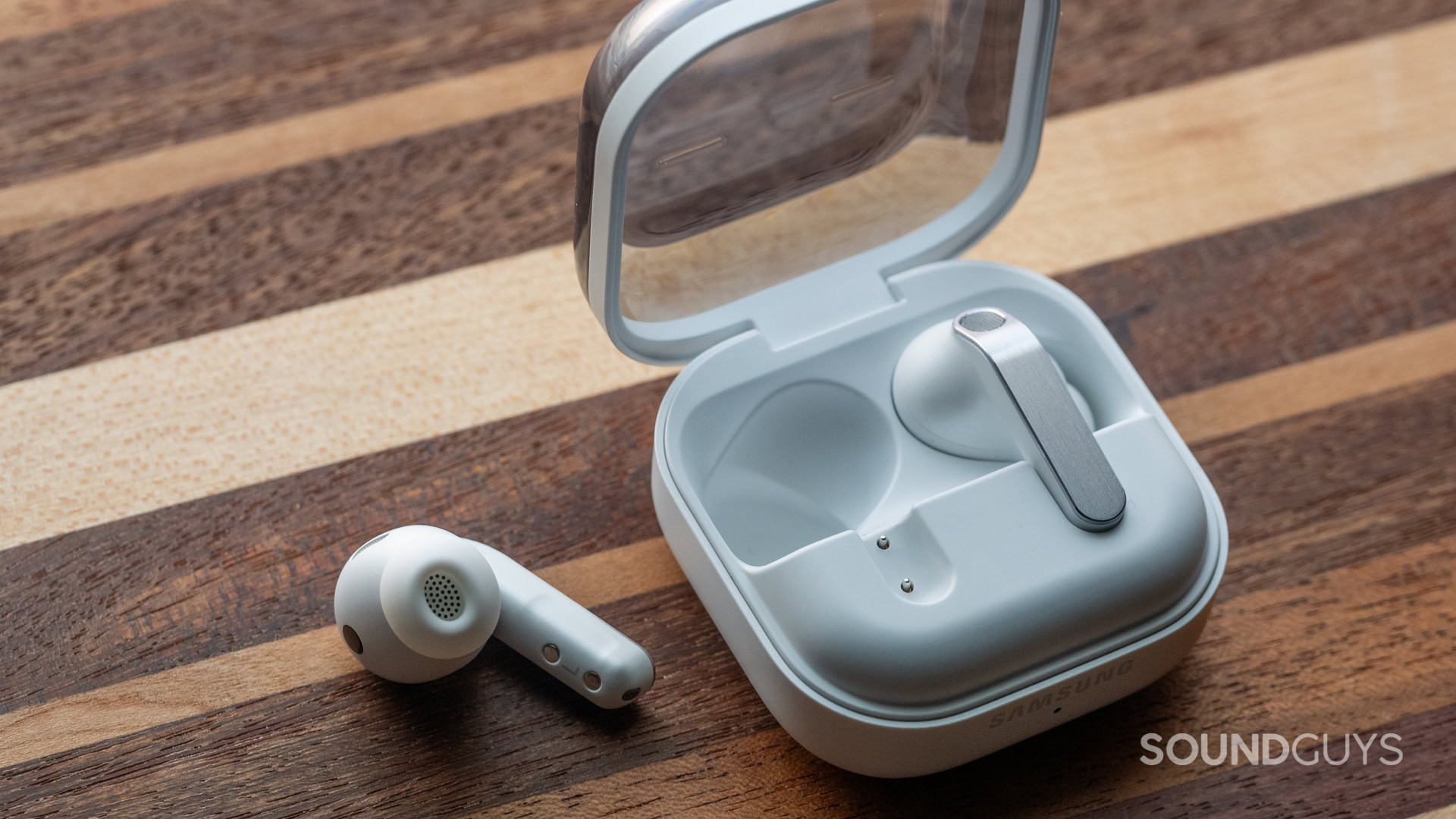 The Samsung Galaxy Buds 4 Pro sitting atop a wooden desk, with one earbud out of the charging case.