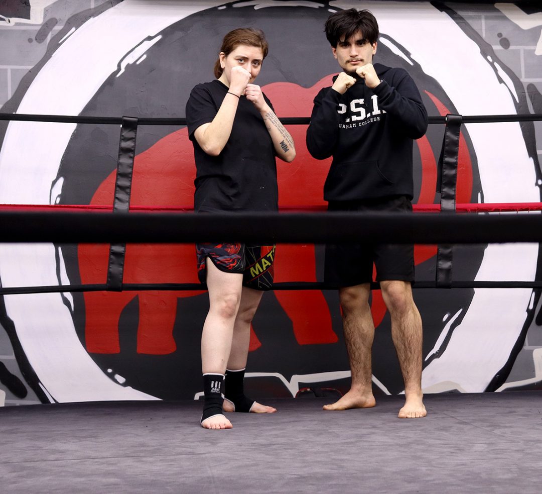 A girl and a boy wearing black shorts and shirts pose inside a combat sports ring.
