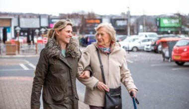 A mature woman help a senior woman out of a car as she takes her to the shops.