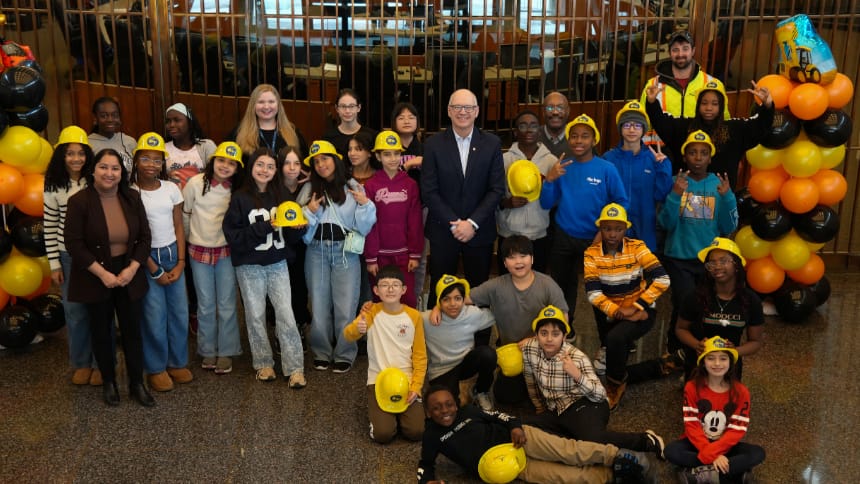 A large group of students wearing yellow hard hats pose with the mayor.