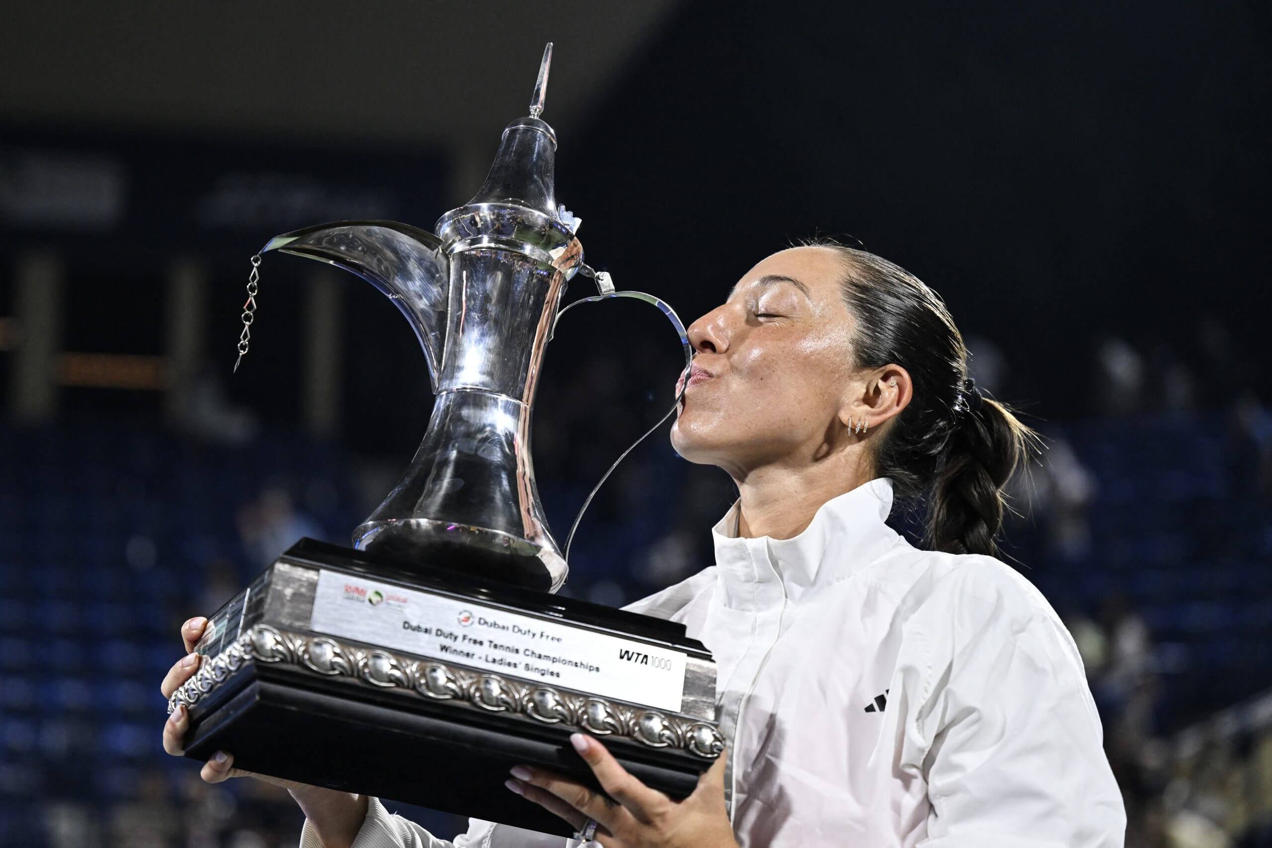 Jessica Pegula kisses a silver trophy in the shape of a traditional Emirati coffee or tea service vessel.
