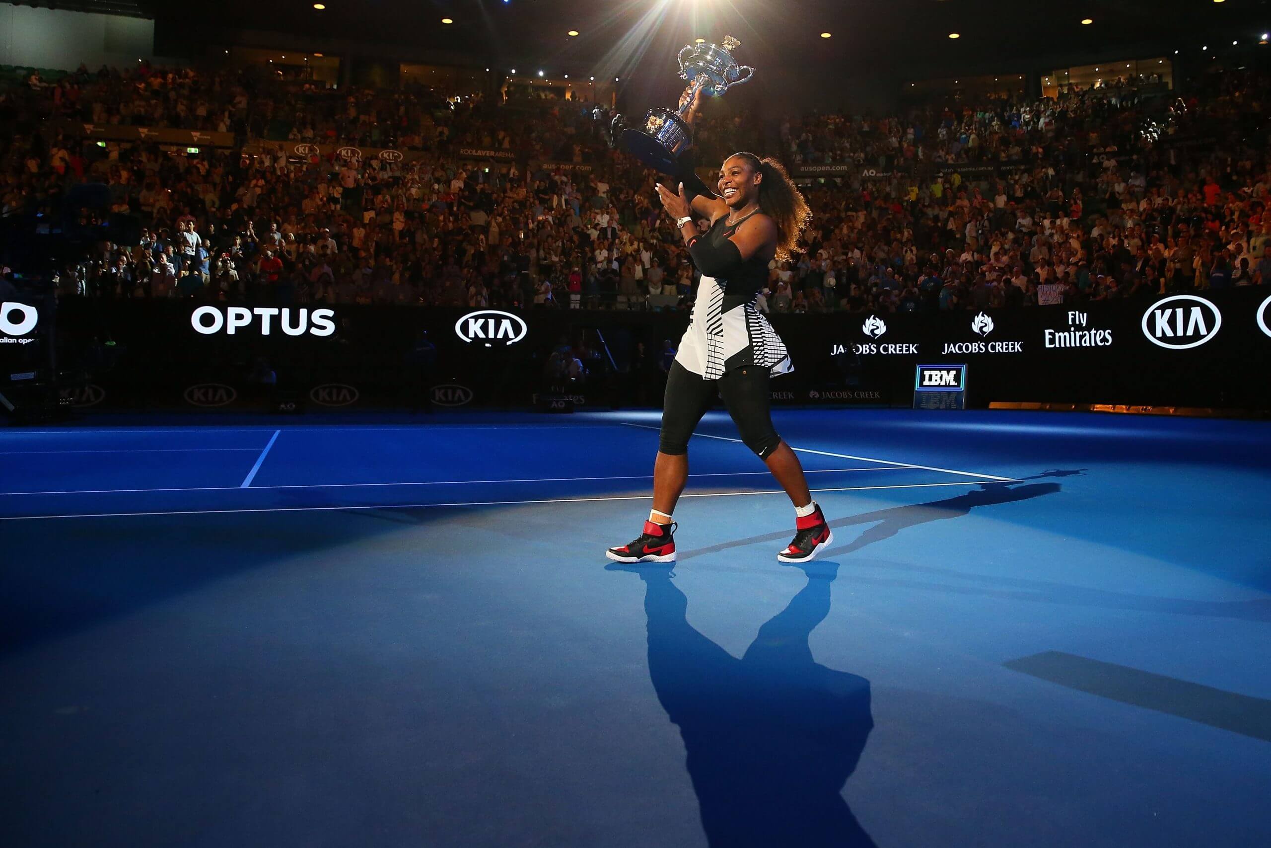 Serena Williams holds the Daphne Akhurst Memorial Cup aloft on a blue tennis court on Rod Laver Arena in Melbourne.