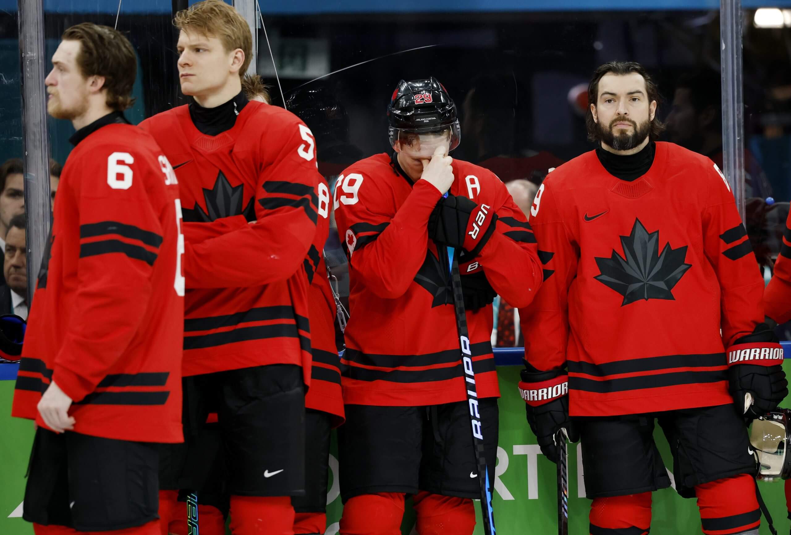 Nathan MacKinnon, surrounded by fellow Team Canada players, is the only one still wearing a helmet and has his face buried in his stick.