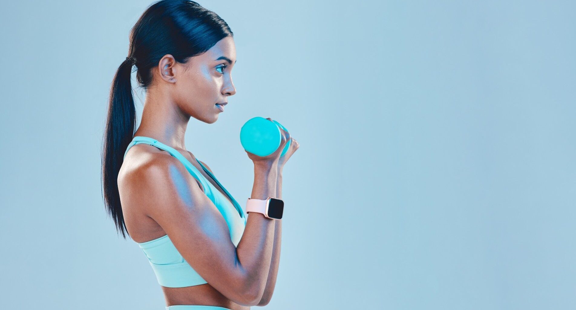 Woman facing side on to camera performing bicep curl with dumbbell