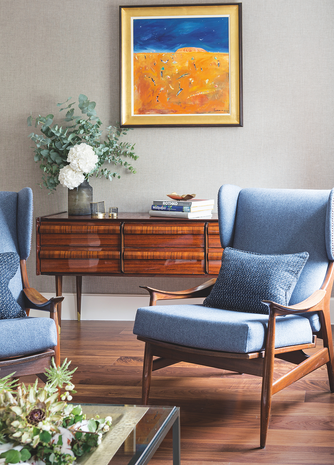 Styled living room with light grey walls walnut wooden flooring and walnut wood armchairs and sideboard