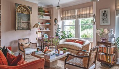 A warm, eclectic living room featuring dusty pink walls, a burnt orange velvet sofa, and woven cane armchairs arranged around a stone coffee table