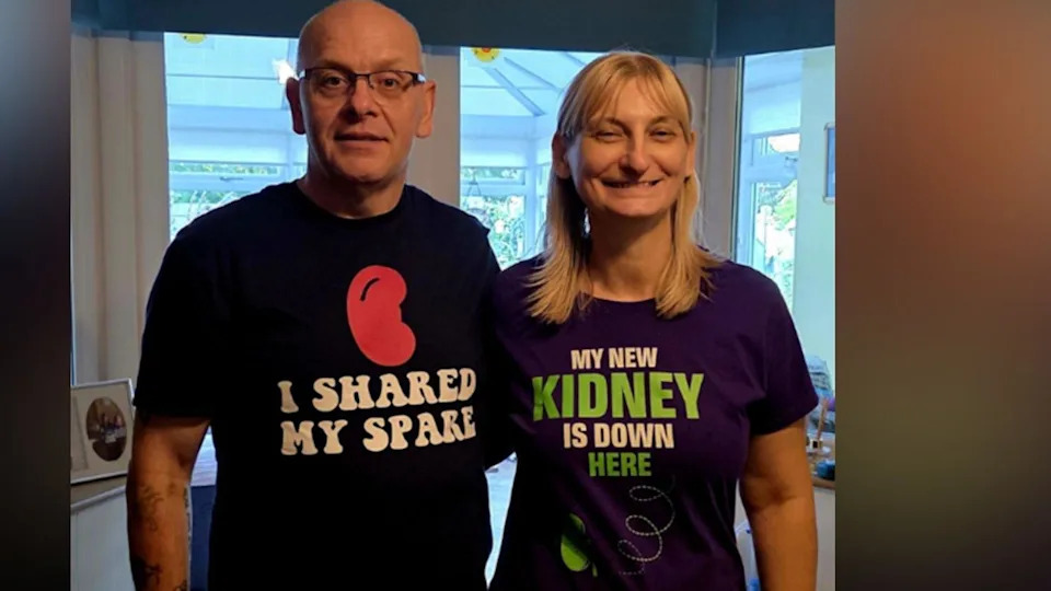 On the left, there is a man who is bald. He is wearing a black t-shirt with a red kidney shape, and the words 'I shared my spare' underneath. To his right, there is a woman with blonder hair. She is wearing a purple t-shirt with white text saying 'my new kidney is down here.' The letters in 'kidney' and 'here' are both in green and there is an arrow pointing to her kidney.