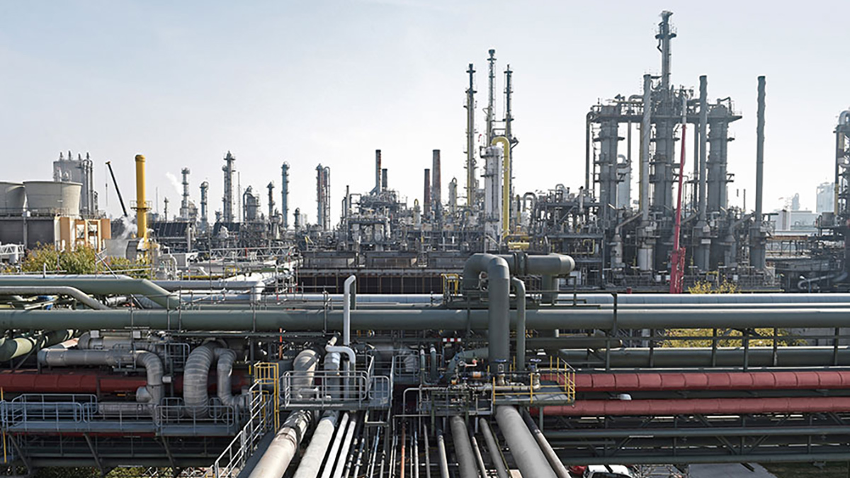 A production plant, consisting of many series of pipes stretching every which way and up into the sky, stretches off into the horizon.