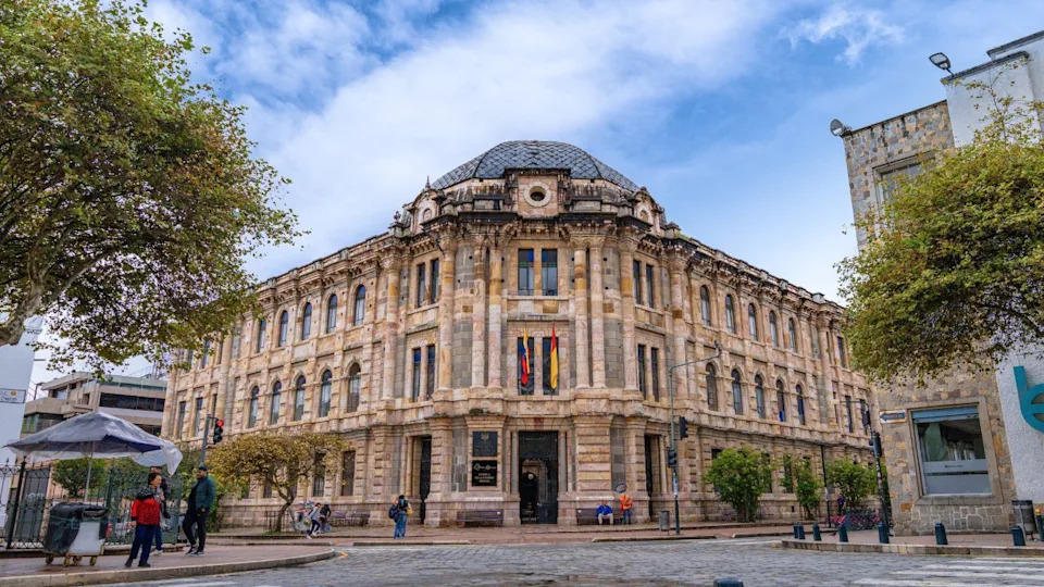 Cuenca, Ecuador – March 1, 2025: Street view of the Provincial Court of Justice of Azuay, an iconic neoclassical building in Cuenca’s historic center, with people walking nearby under a partly cloudy