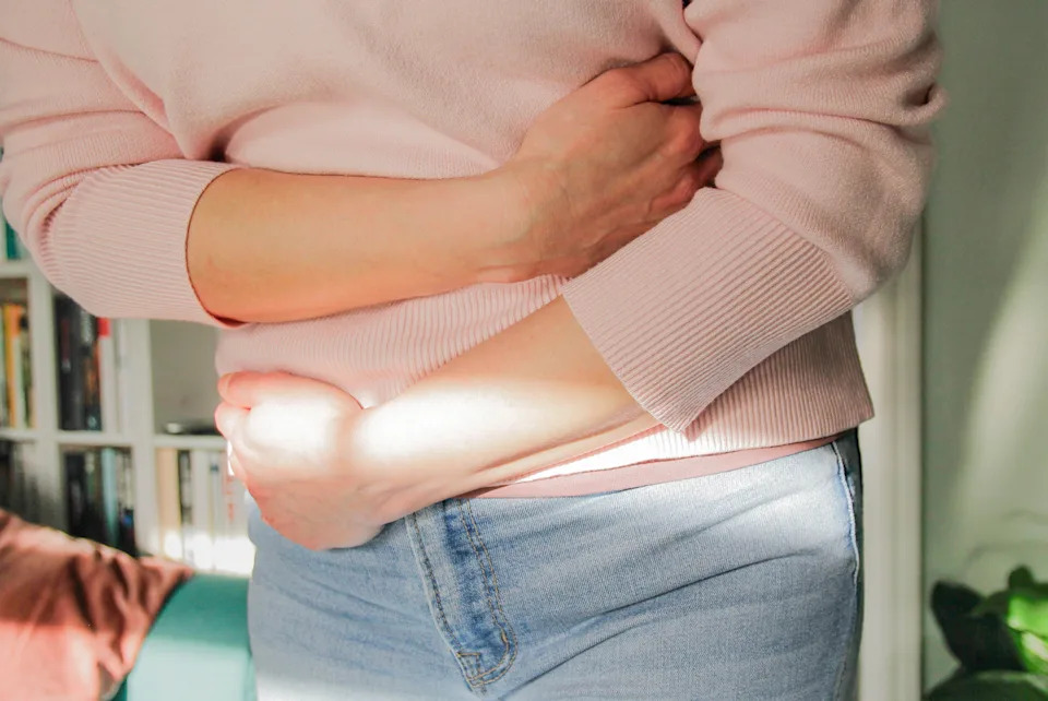 A woman wraps her hands around her stomach, as she might be dealing with abdominal pain due to colorectal cancer.