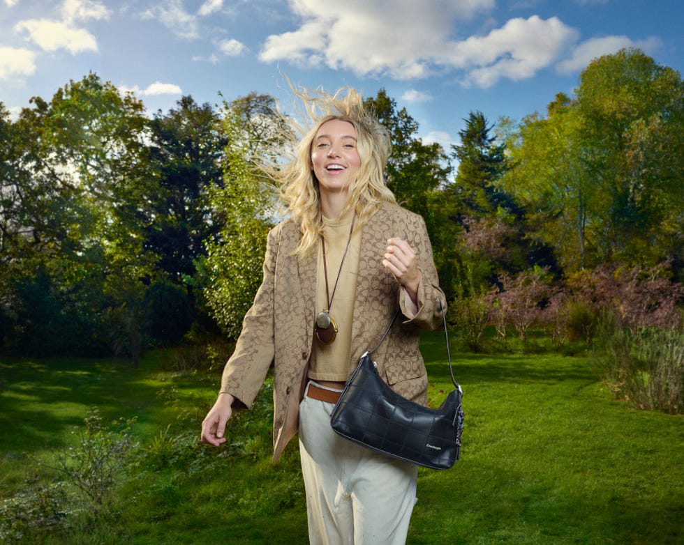 a person walking through a grassy area with trees in the background wearing a stylish outfit