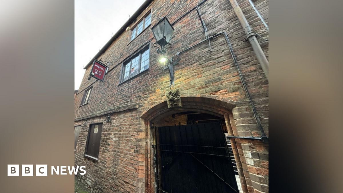 An old gatehouse in a town centre, a three-storey brick building with a large arch.