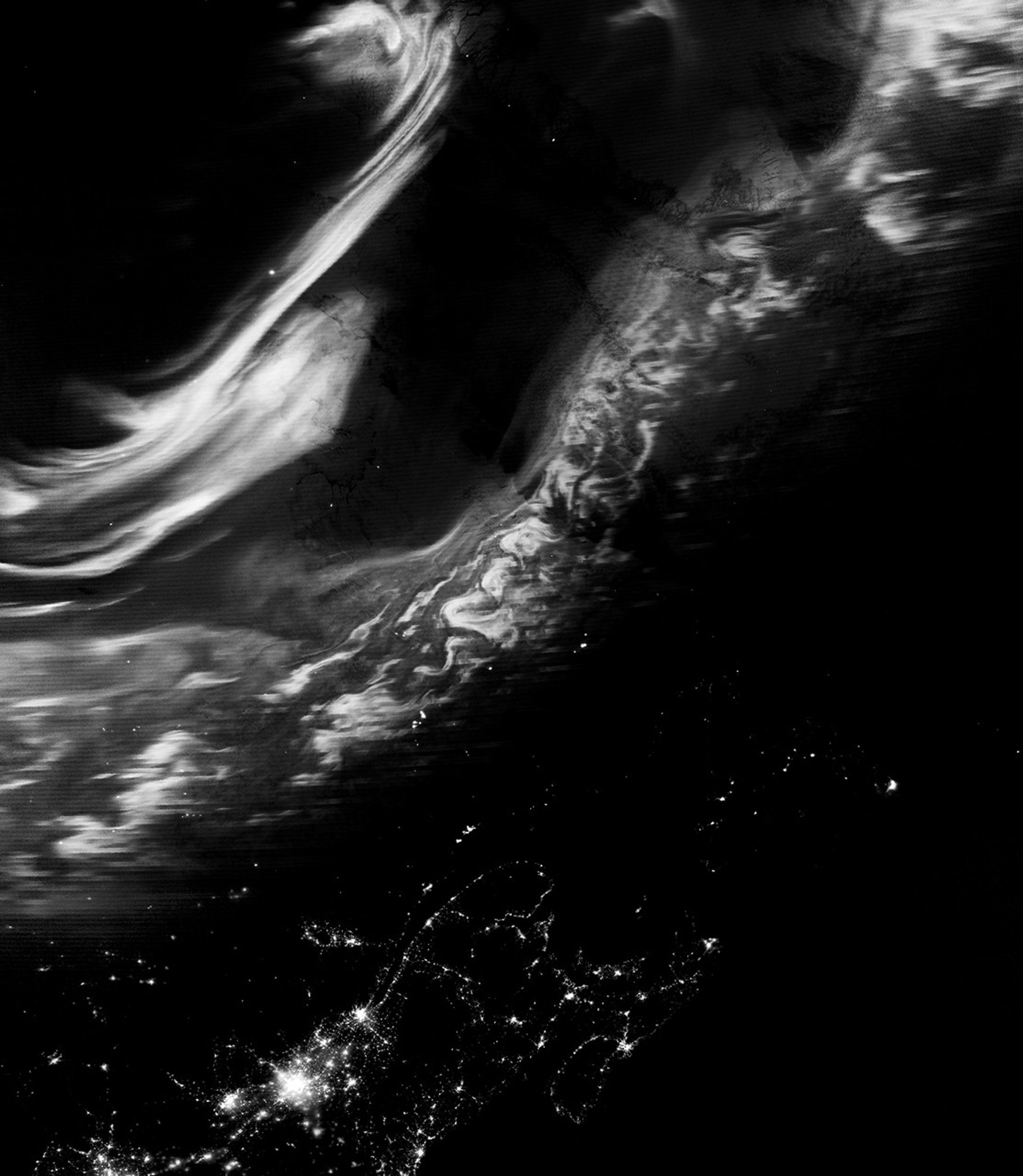 A nighttime satellite image shows a grayscale view of the northern lights stretching from eastern Canada to southern Greenland. Urban light from Montreal and nearby cities appear across the bottom of the scene.