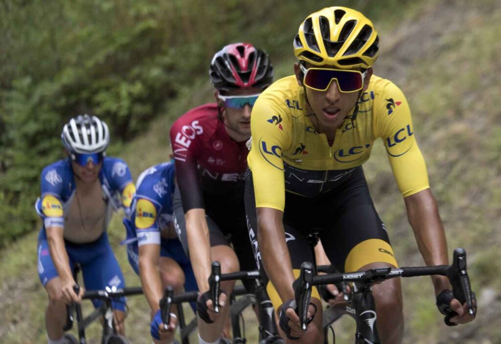 Egan Bernal riding in the yellow jersey during the 2019 Tour de France, surrounded by fans and riders.