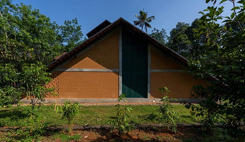a semi-circular porous brick house stands amid rubber plantation in india