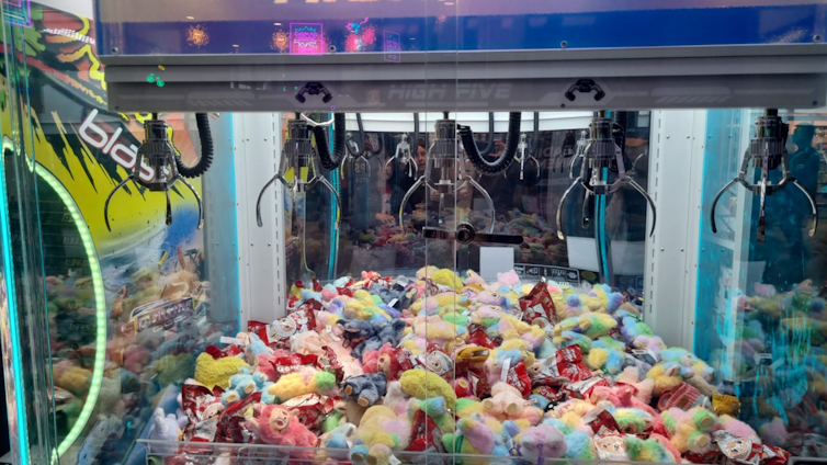 Close-up view of a claw machine with several claws, filled with a wide variety of colourful toys.