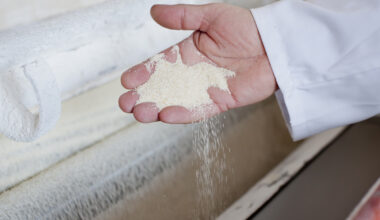 The hand of a man wearing a white coat scoops some flour from a bin in a milling facility.