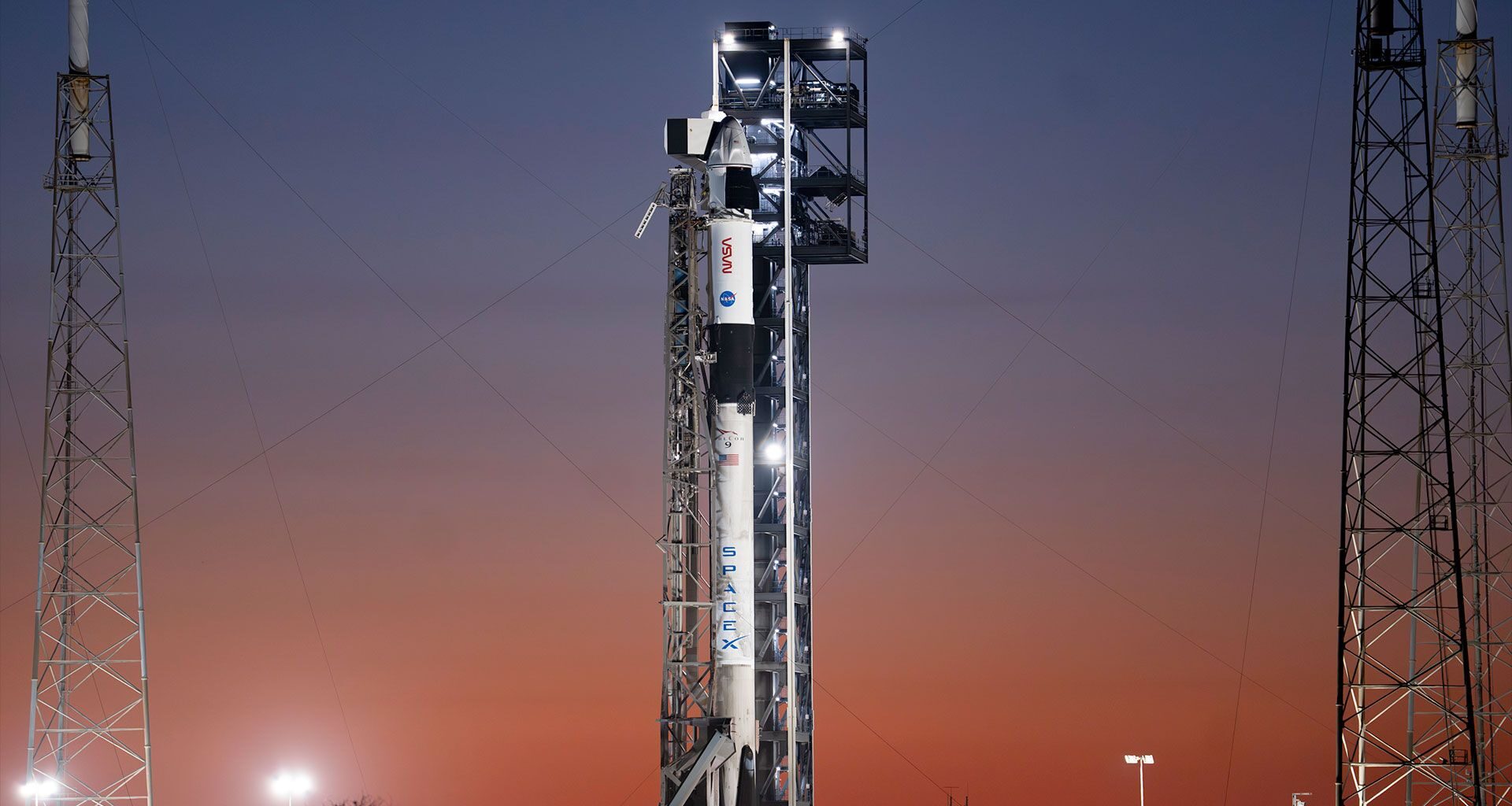 Backdropped by the sunrise, a white and black rocket stands poised on its launch pad