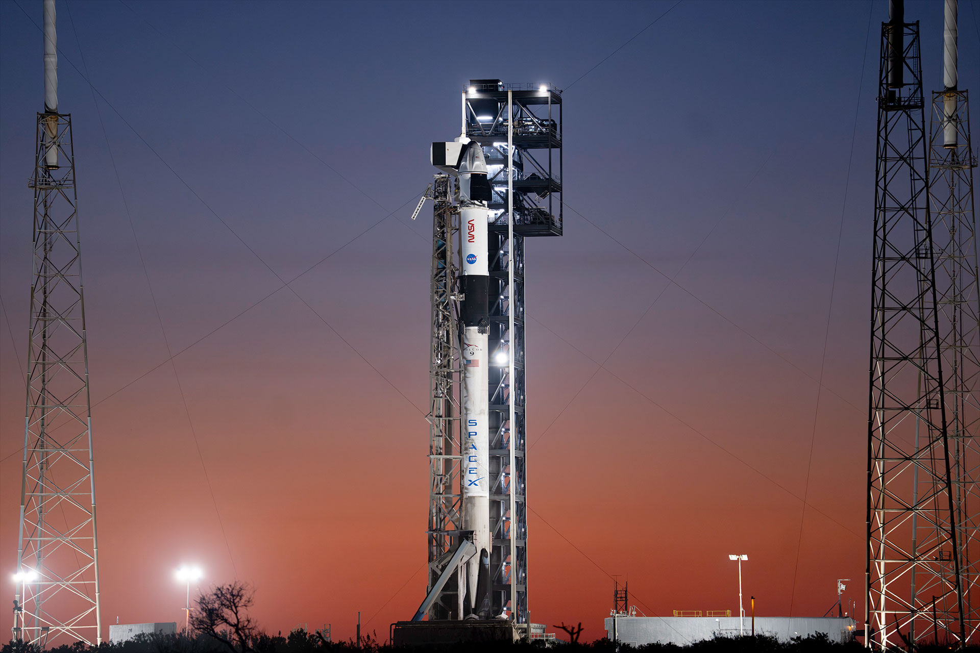 Backdropped by the sunrise, a white and black rocket stands poised on its launch pad
