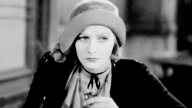 Greta Garbo as Anna Christie holding a full shot glass and wearing a hat in Anna Christie