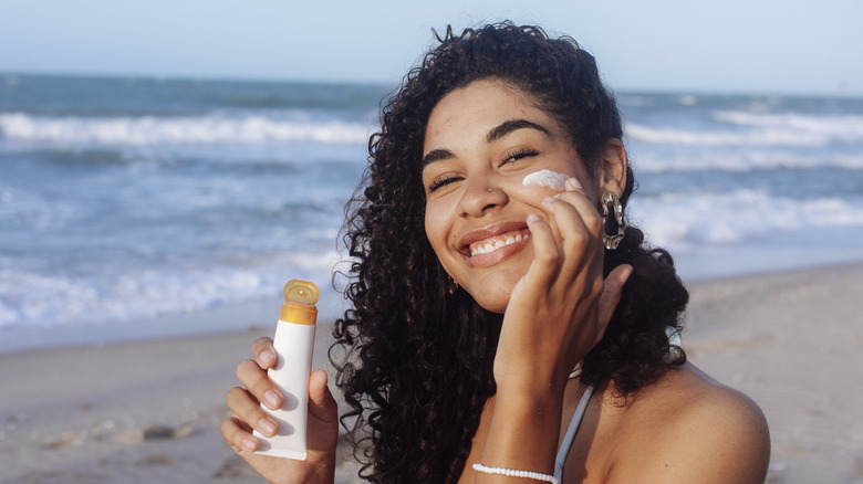 woman applying sunscreen to face on a beach