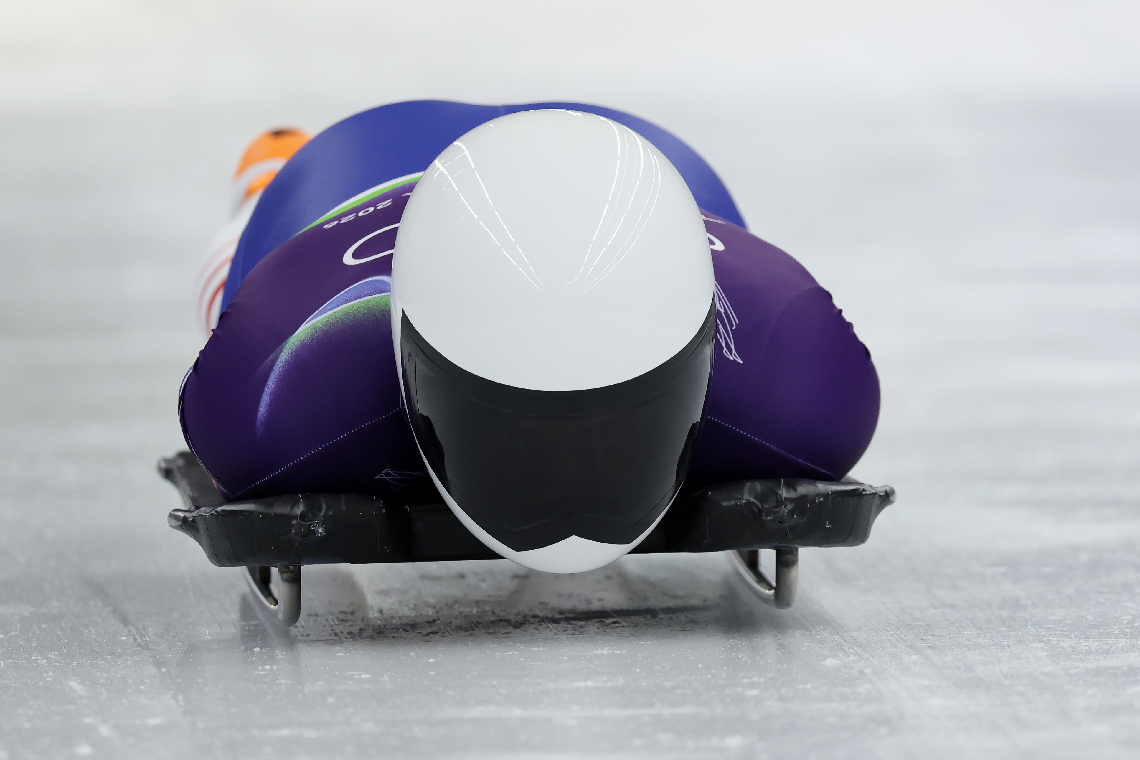A front-on closeup of a helmeted athlete competing in the skeleton