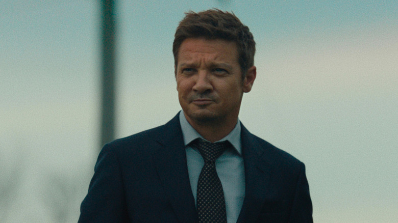 Mike McLusky (Jeremy Renner) smirks while standing wearing a suit in Mayor of Kingstown