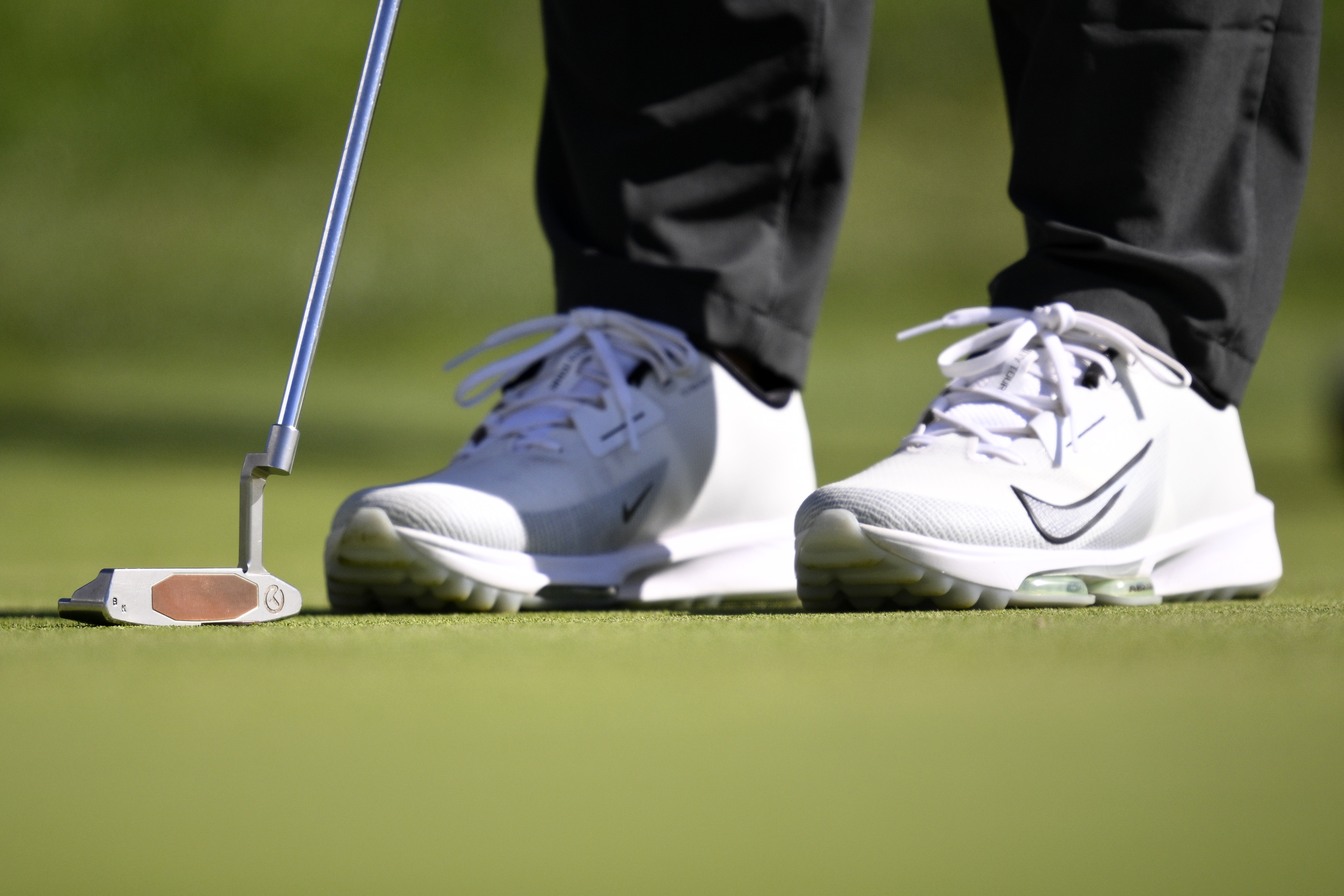 A close up of Brooks Koepka's white Nike shoes and Scotty Cameron Newport 2 putter