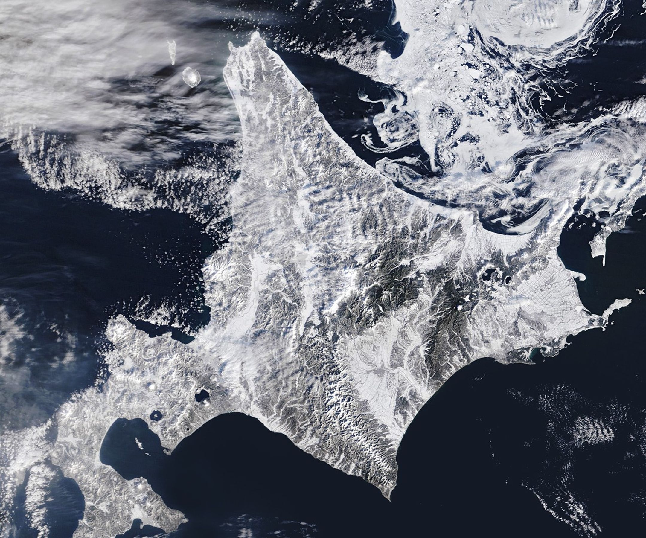 A satellite image shows snow blanketing Hokkaido, Japan, with sea ice swirling just north of the island.