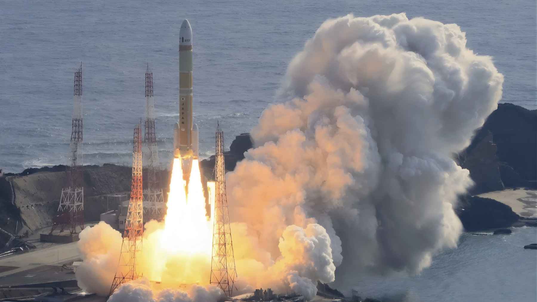 Japan's H3 rocket lifts off from Tanegashima Space Center, flames and smoke rising over the Pacific.