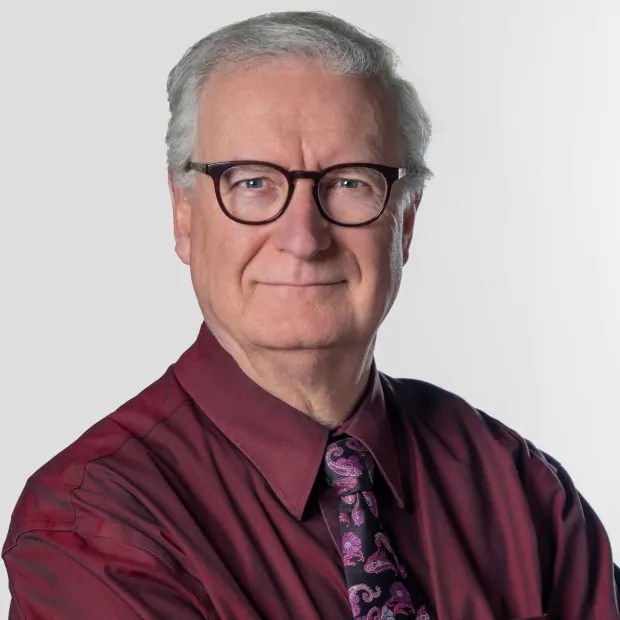 A grey haired white man in a dress shirt, tie and glasses.
