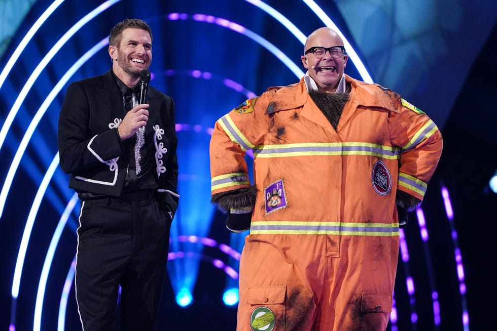 two individuals on stage one holding a microphone and the other in a firefighter costume