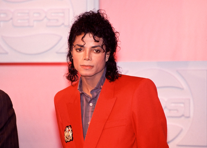 Michael Jackson wearing a red blazer with curly black hair at a promotional event, linked to secret tapes on children. Michael Jackson wearing a red blazer with curly black hair at a promotional event, linked to secret tapes on children.