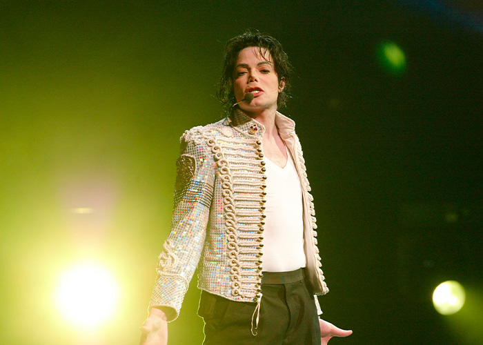 Michael Jackson performing on stage wearing a sequined military jacket with lighting highlighting his presence. Michael Jackson performing on stage wearing a sequined military jacket with lighting highlighting his presence.