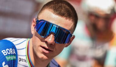 A close-up shot of Remco Evenepoel wearing large sunglasses and wearing the Red Bull-Bora-Hansgrohe kit with rainbow trim on the collar