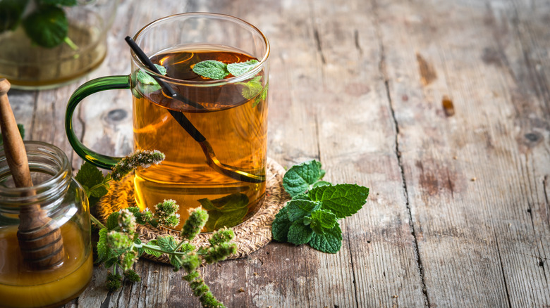 A mug of peppermint tea surrounded by peppermint leaves on a wooden table