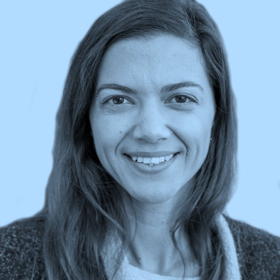 Person with long hair wearing a sweater and light-colored top against a blue background.