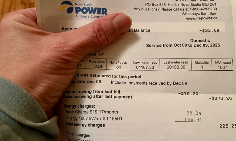 A Nova Scotia Power bill is held in a white person's hand showing total energy charges of $225.25.