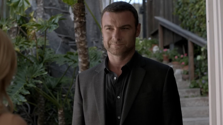 Ray Donovan (Liev Schreiber) stands smiling looking at a woman by a set of stairs in Ray Donovan