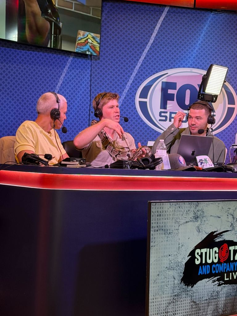 Robert Irwin on a radio show with a snake around his arm.