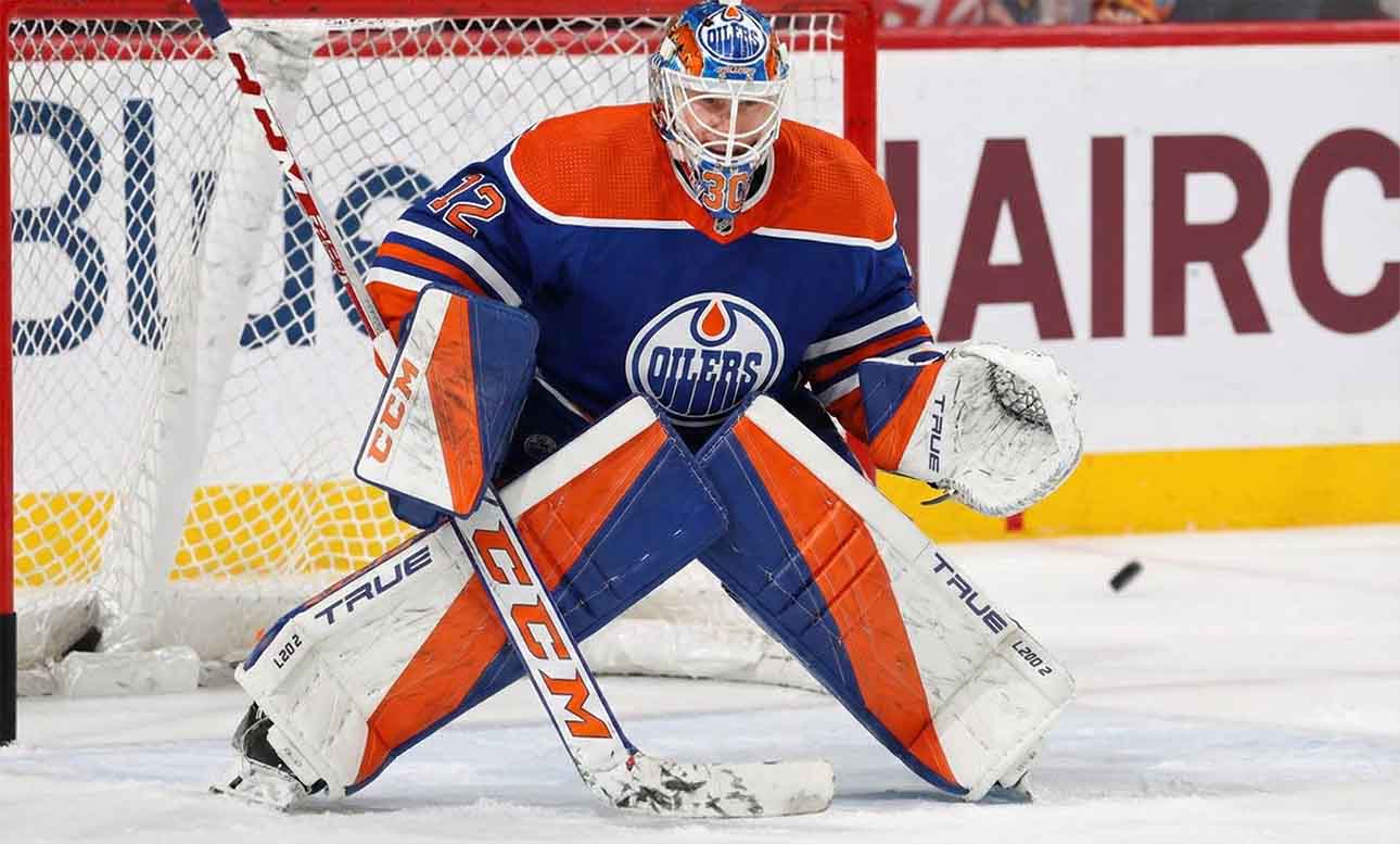 Sergei Bobrovsky crouched in a butterfly stance guarding the net, wearing a full Edmonton Oilers goaltender uniform including a blue and orange jersey, custom-painted mask, and matching pads with a puck visible near his glove.