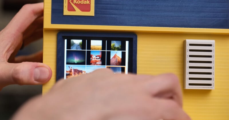 Close-up of hands operating a yellow and blue Kodak device with a small digital screen displaying a grid of colorful thumbnail images.