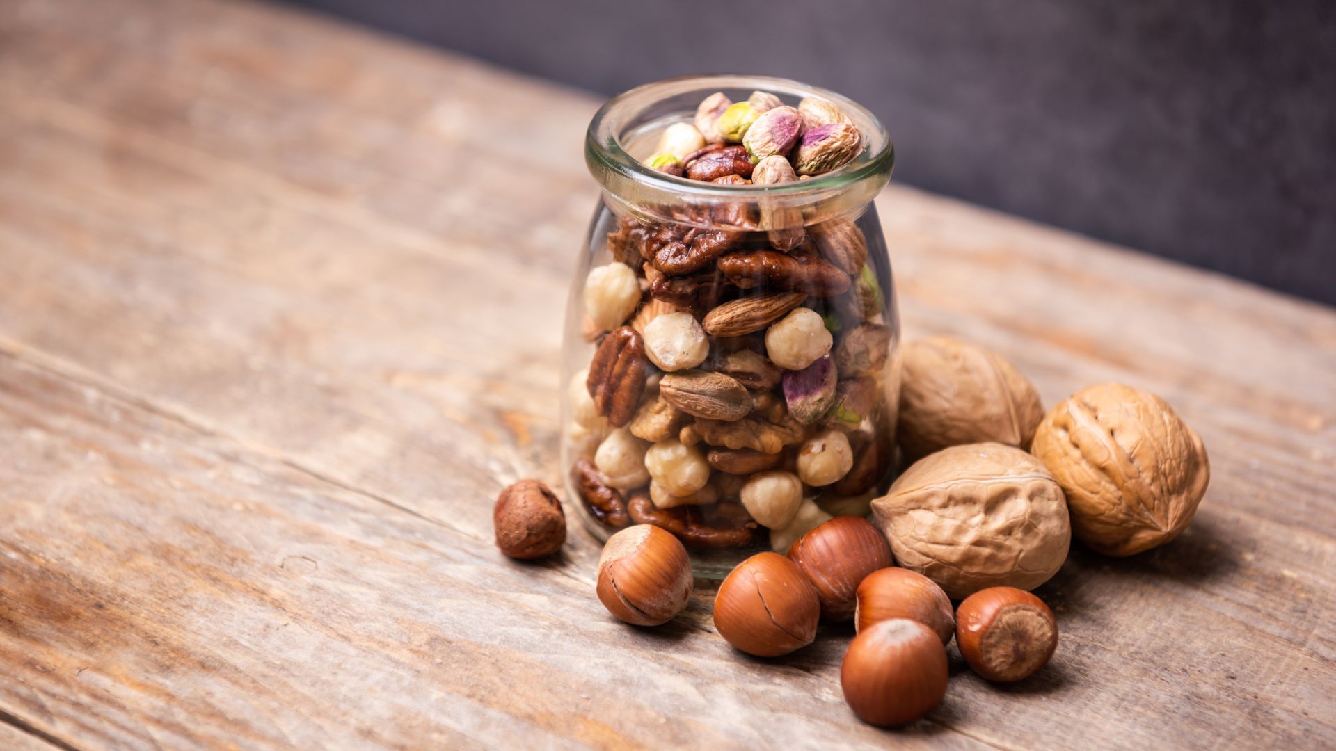 A glass jar full of different types of nuts on a wooden table