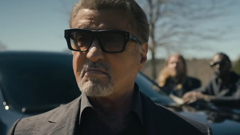 Dwight Manfredi (Sylvester Stallone) stands by an SUV wearing tinted glasses in Tulsa King