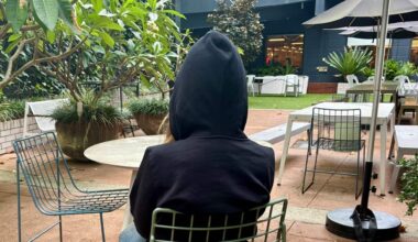 A person wearing a black hooded jacket sits in a courtyard.