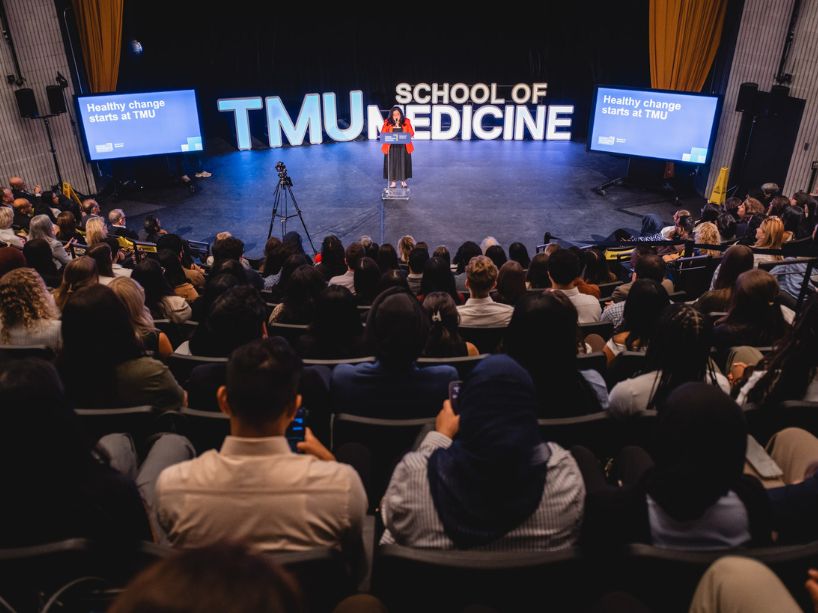 A woman standing at a podium at the centre of an auditorium.