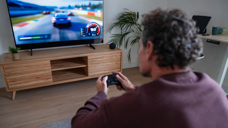 Man holding a game controller and playing a racing game on a TV