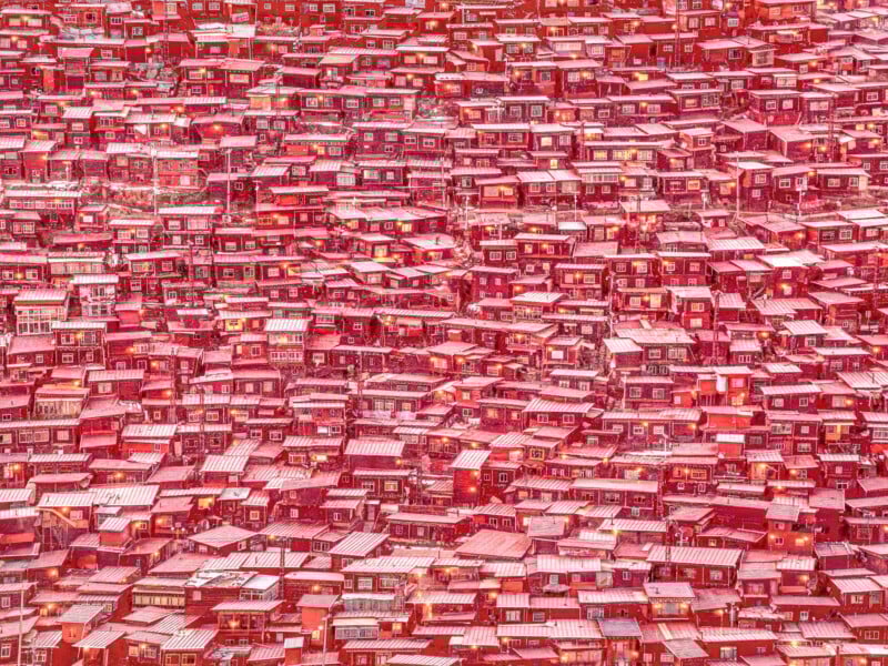A dense cluster of red-roofed houses closely packed together on a hillside, creating a vibrant, intricate pattern with little visible space between the buildings.
