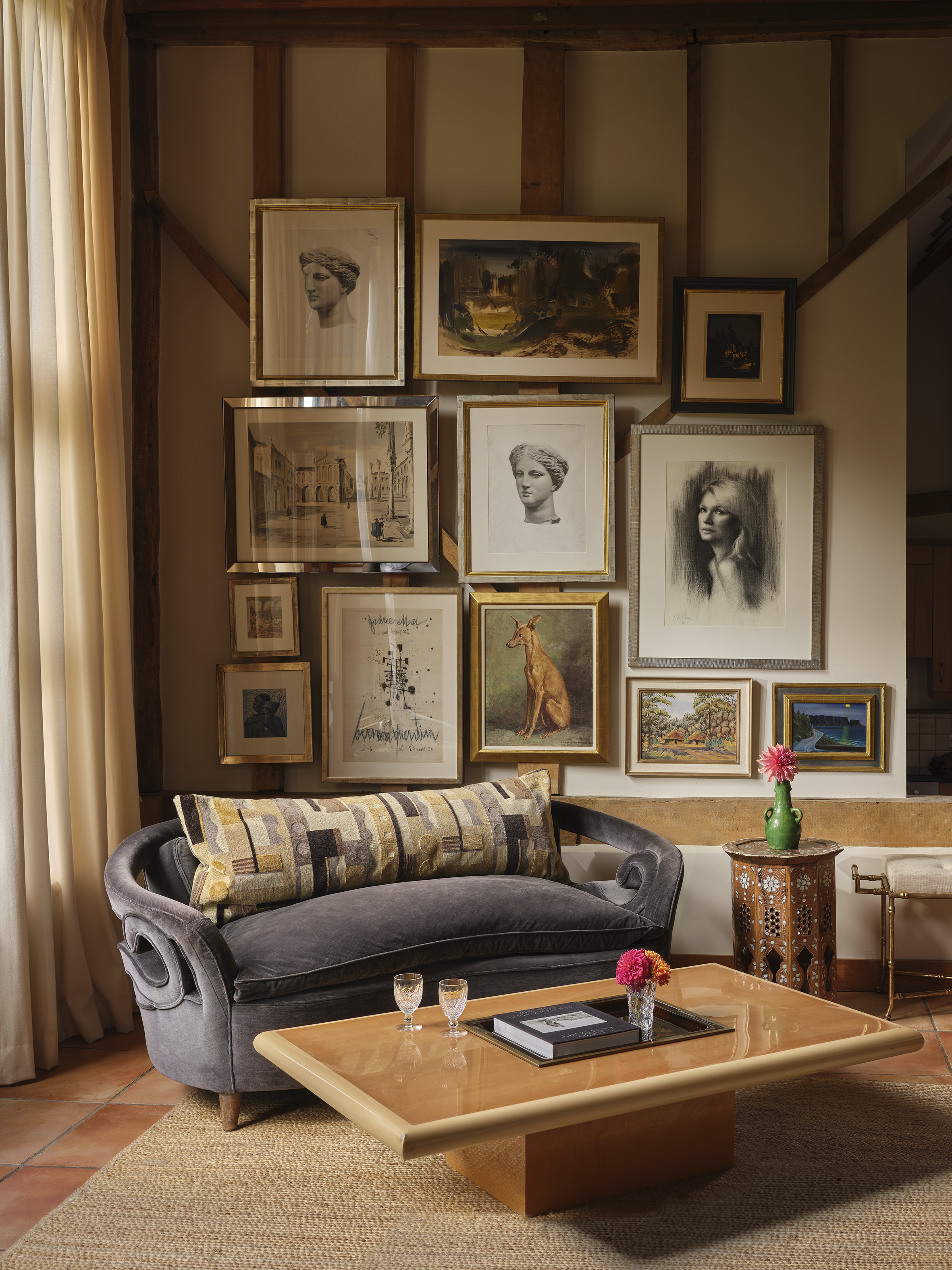 A cozy living room with a dark velvet sofa, a light wood coffee table, and a wall of framed art.