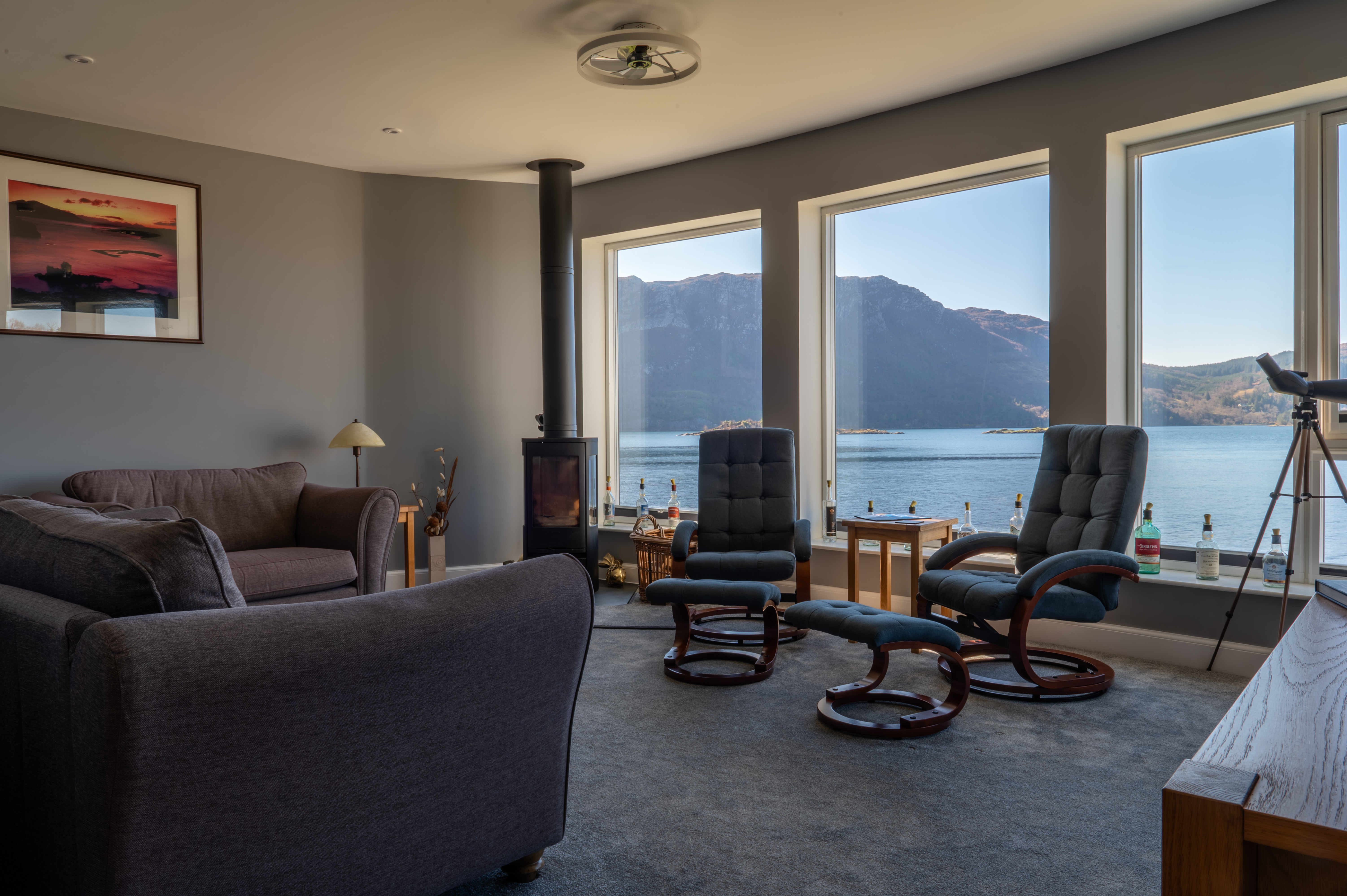 A living room with large windows overlooking a body of water and mountains.